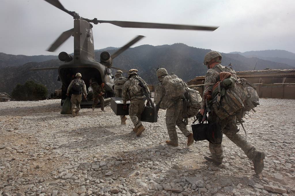 U.S. soldiers board an Army Chinook transport helicopter in Afghanistan, surrounded by mountain peaks.