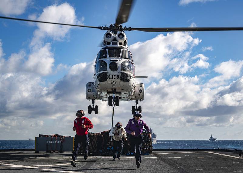 Sailors run past the foul line as a SA-330J Puma picks up pallets from the flight deck of the amphibious dock landing ship USS Ashland (LSD 48) on June 25, 2019, prior to a replenishment-at-sea with the amphibious assault ship USS Wasp (LHD 1) and fleet replenishment oiler USNS Rappahannock (T-AO 204).