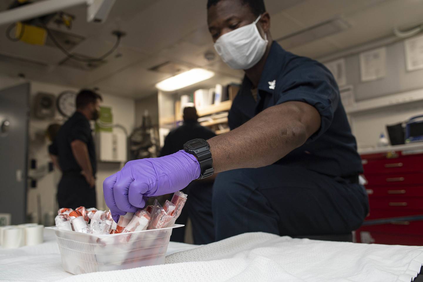 Hospital Corpsman 2nd Class Eric Hayford collects sealed COVID-19 test samples aboard the amphibious transport dock ship USS New Orleans (LPD 18) on Aug. 12, 2020, in the Sea of Japan.