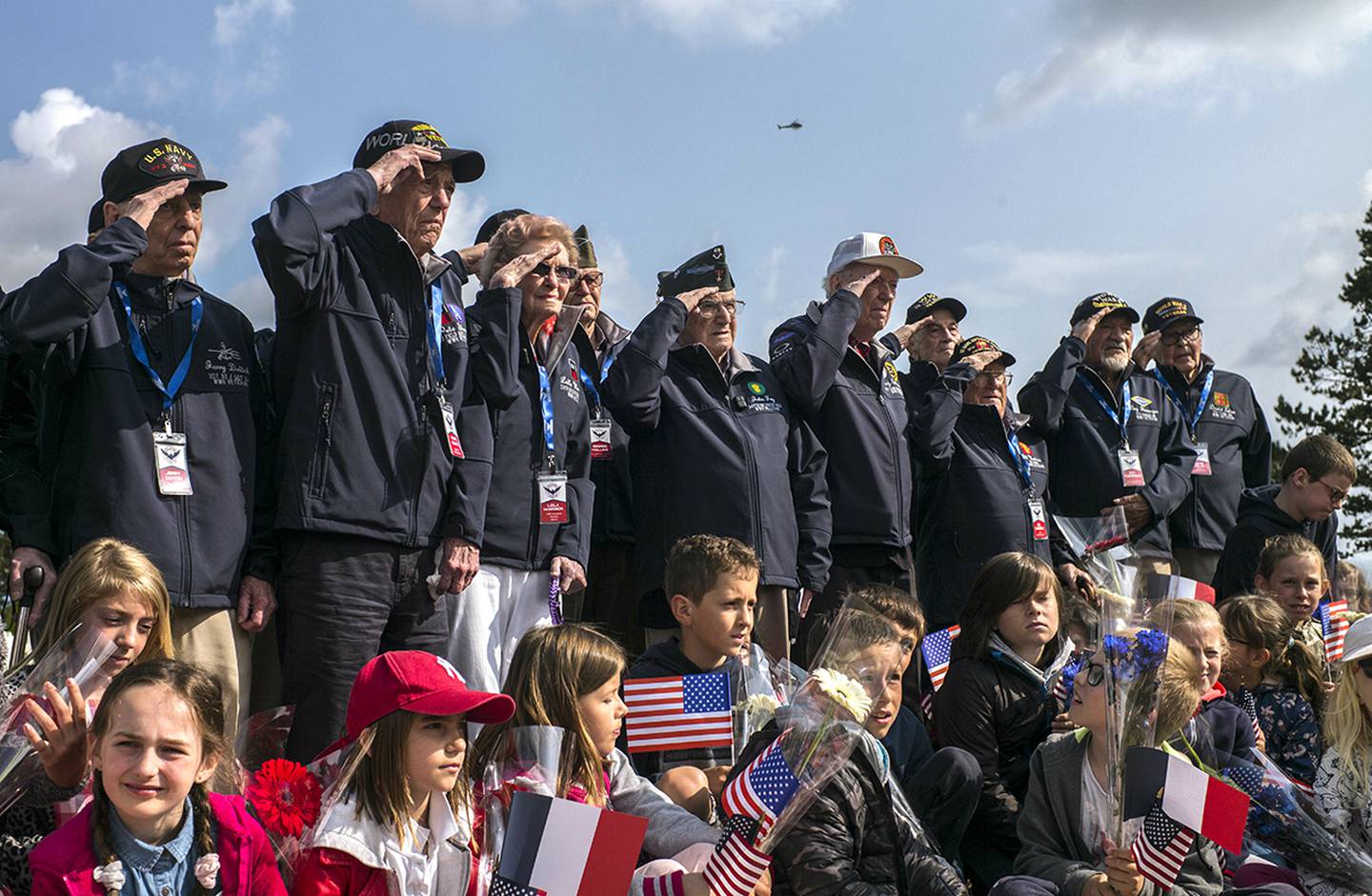 World War II veterans from the United States salute as they pose with local school children at the Normandy American Cemetery in Colleville-sur-Mer, Normandy, France