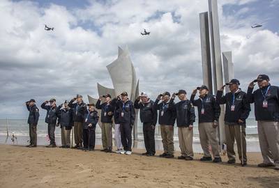 World War II veterans from the United States salute as they pose in front of Les Braves monument at Omaha Beach in Saint-Laurent-sur-Mer, Normandy, France