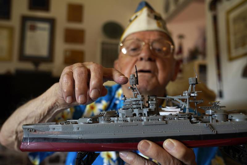 Mickey Ganitch holds up a model of the USS Pennsylvania and points to where he served as a lookout during the 1941 attack on Pearl Harbor, in the living room of his home in San Leandro, Calif., Nov. 20, 2020.