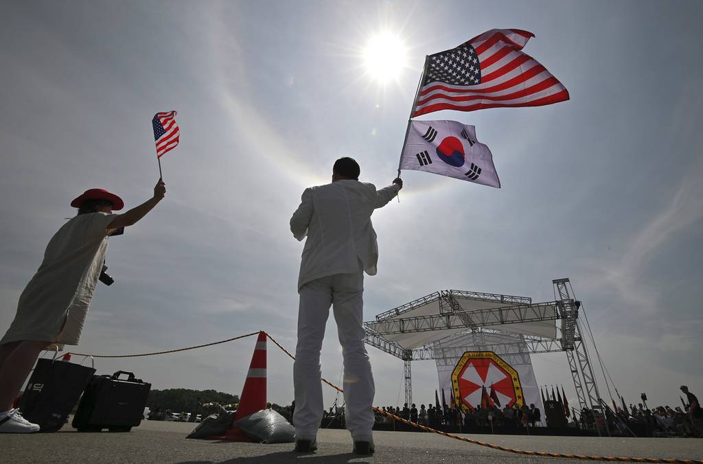 A man and a woman wave flags during a ceremony to commemorate the 75th anniversary of the Eighth U.S. Army at Camp Humphreys in Pyeongtaek on June 8, 2019.