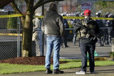An armed supporter of President Donald Trump looks in at a gathering of Washington State Patrol troopers behind a perimeter fence during a rally, Sunday, Jan. 10, 2021, at the Capitol in Olympia, Wash.