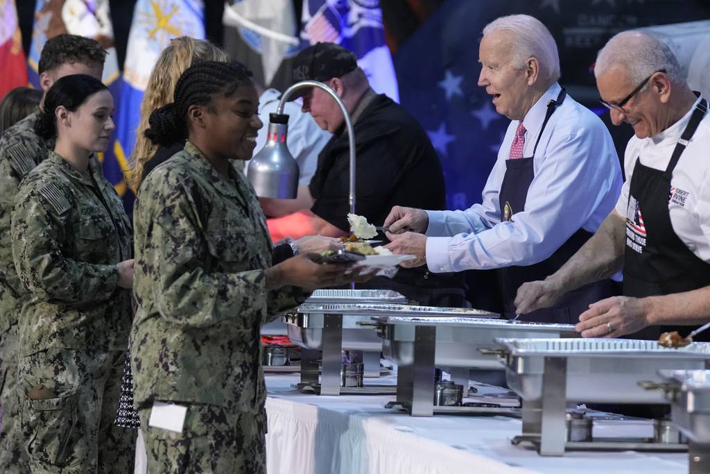 President Joe Biden and chef Robert Irvine, right, help serve a "friendsgiving" meal to service members and their relatives at the Norfolk Naval Station on Sunday, Nov. 19, 2023, in Norfolk, Va.