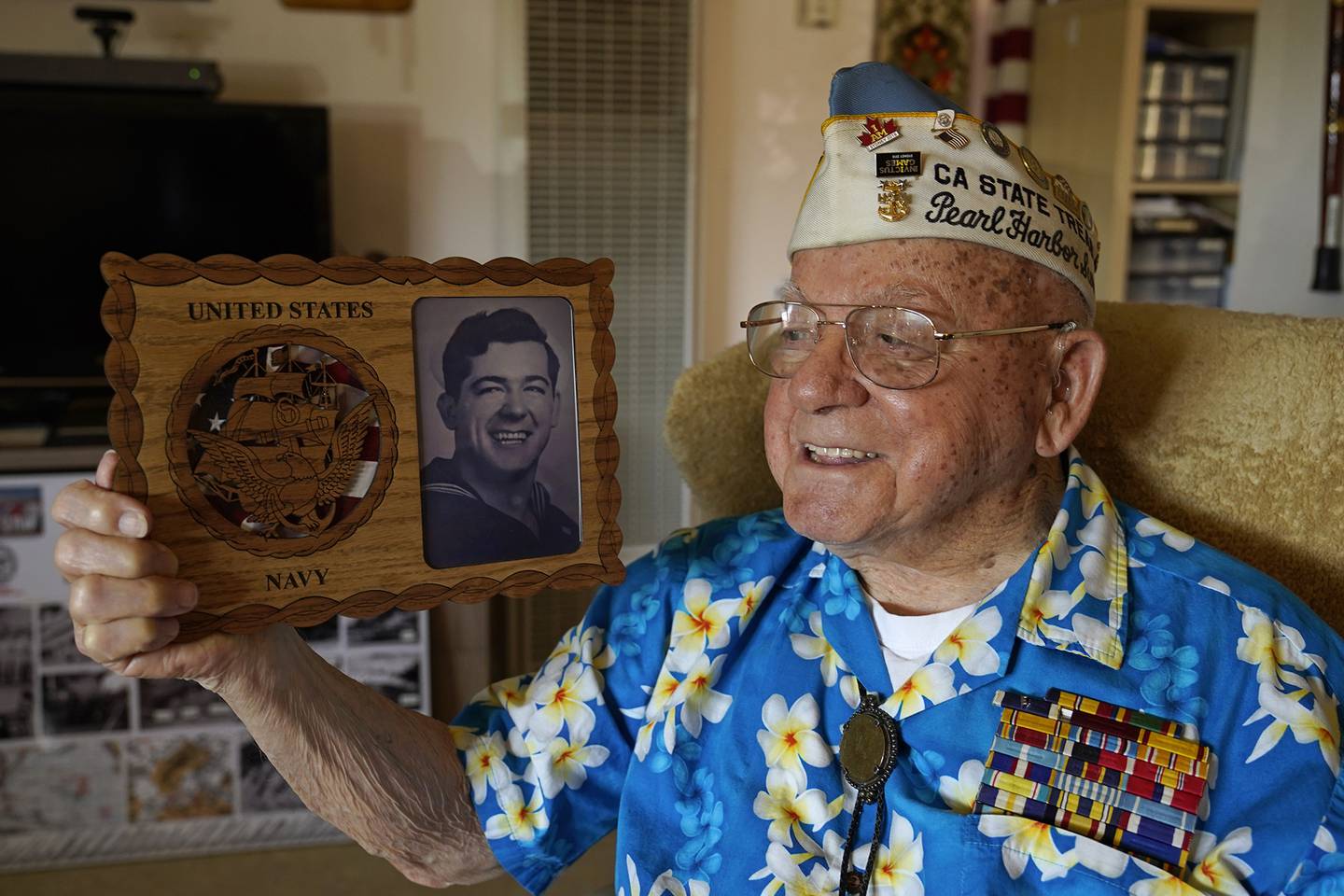 Mickey Ganitch, a survivor of the 1941 attack on Pearl Harbor, holds a plaque with a picture of himself as a young sailor, while sitting in the living room of his home in San Leandro, Calif. Nov. 20, 2020.