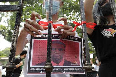 A demonstrator ties a red ribbon on a gate of the Department of Justice to symbolize their protest while holding a picture of U.S. Marine Lance Cpl. Joseph Scott Pemberton during a rally in Manila, Philippines, on Thursday, Sept. 3, 2020.